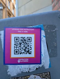 Street sticker A square sticker featuring a vibrant magenta background with a blue outer border. Inside, an orange border frames a white square containing a black QR code. Above the QR code, white text asks 'LOOKING FOR INSPIRATION? FIND IT HERE:'. Below the QR code, also in white text, is the phrase 'INSPIRATION GATHERED' accompanied by a stylized white logo resembling a 'Y' or a sprouting leaf. The sticker is affixed to a grey, textured surface, partially overlapping older, torn stickers.