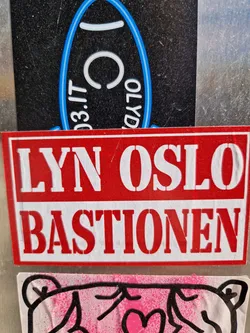 Street sticker A red and white sticker with the text "LYN OSLO BASTIONEN" in a stencil-like font. It's affixed to a surface with other stickers visible in the background.