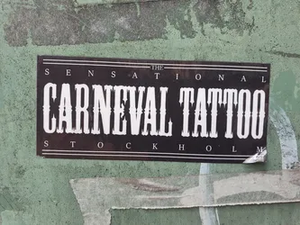 Street sticker A black and white sticker with the text "The Sensational Carnival Tattoo Stockholm" in a bold, western-style font. The sticker is affixed to a weathered green wall.