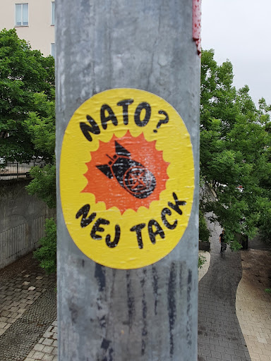 Street sticker A yellow round sticker with a black and orange illustration of a bomb with wings. The text NATO? Nej tack is visible on the sticker. Nej tack is Swedish for No thanks. 