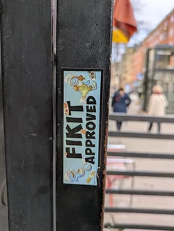 Street sticker The sticker is adhered to a black metal surface. It features a light blue background with a cartoon rabbit in overalls. Above the rabbit is the text 'FIKIT APPROVED' in bold black letters.