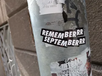 A black die-cut sticker featuring bold white sans-serif text stacked in two lines: 'REMEMBERRR' and 'SEPTEMBERRR'. It is pasted on a weathered metal pole.