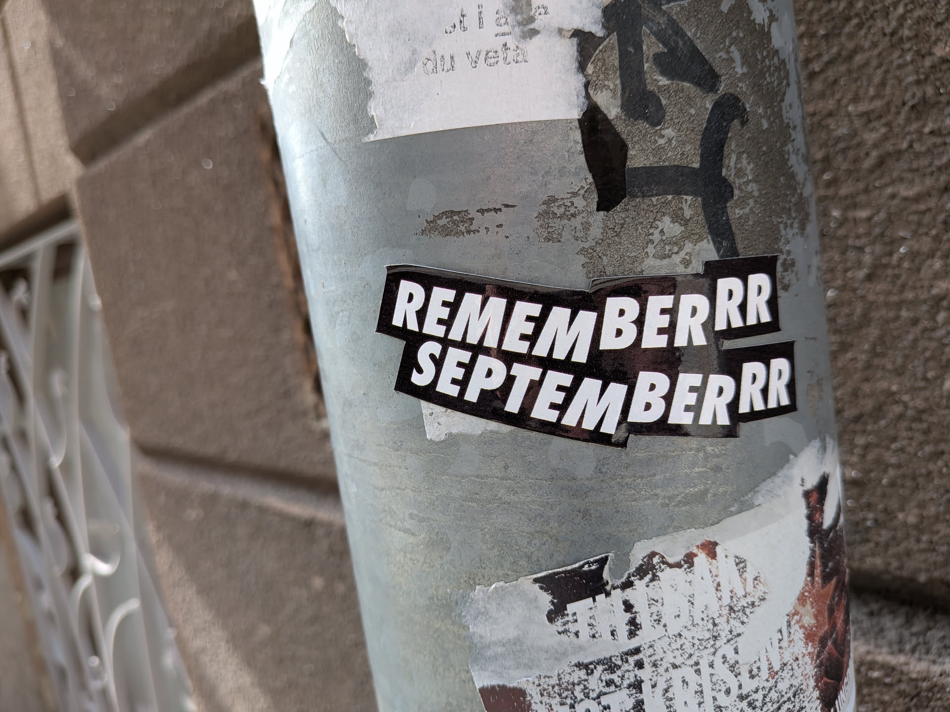 A black die-cut sticker featuring bold white sans-serif text stacked in two lines: 'REMEMBERRR' and 'SEPTEMBERRR'. It is pasted on a weathered metal pole.