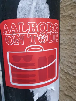 Street sticker Red sticker with the text "Aalborg On Tour" and an illustration of a travel bag with sunglasses and cans inside. 