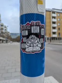 Street sticker The sticker features a cartoonish, somewhat disheveled character with large, tired eyes and messy dark hair, holding their hands over their ears as if to block out noise. They are seated, looking down at an open book. On the right page of the book, a chemical structure (resembling a benzene ring with an attached nitrogen group) is drawn. Surrounding the character's head are multiple old-style television screens, each displaying a distinct QR code. The overall color scheme is predominantly black and white, with a vibrant red outline around the entire sticker and red accents on the text at the top. The text 'LITTLE TEEVEE' is prominently displayed above the character and screens.