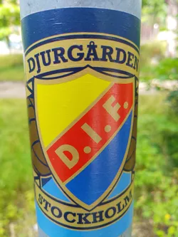 Street sticker A sticker featuring the Djurgårdens IF logo. The logo is a shield divided into yellow, red, and blue sections, with the initials "D.I.F." in the center. The words "DJURGÅRDEN" and "STOCKHOLM" are written at the top and bottom of the sticker respectively.