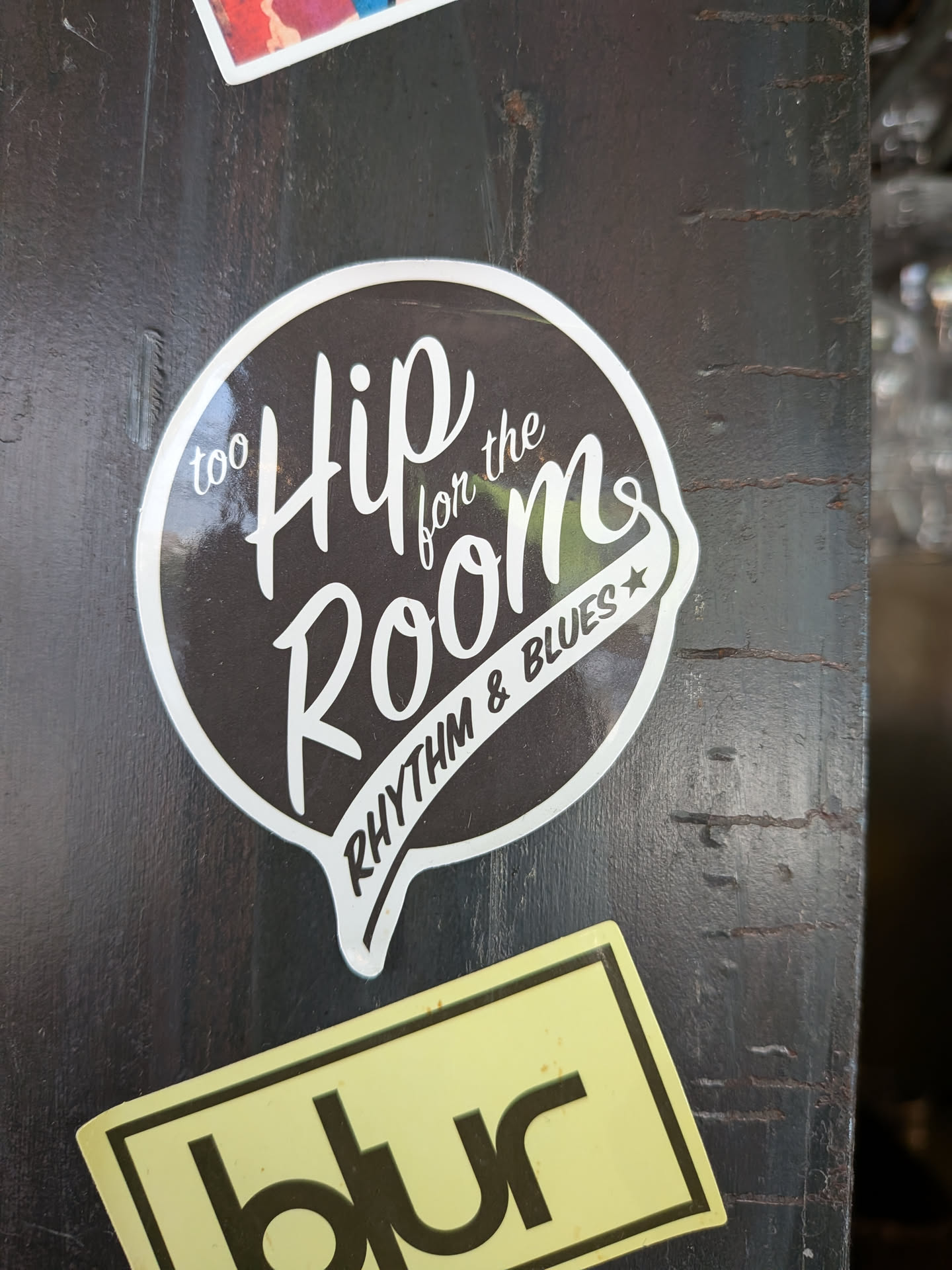 A speech-bubble-shaped sticker featuring a black background with a white border. The center contains stylized white script text reading 'too Hip for the Room', with 'RHYTHM & BLUES' printed along the bottom curve next to a small star.