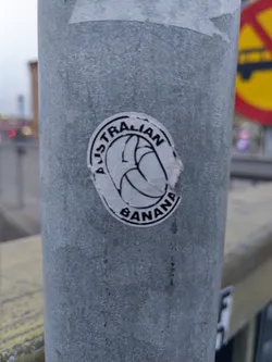 Street sticker A round sticker featuring a stylized banana with the text "Australian Banana" encircling it.  The sticker is affixed to a metal pole.