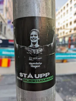Street sticker A black and white image of a young man with his arms raised in victory. He is wearing a sports jersey with the number 13. The text at the bottom of the sticker says "Stå upp som Blickhammar", which translates from Swedish to "Stand up as Blickhammar". The Hemköp Hagen logo is visible.