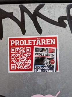 Street sticker A rectangular sticker with a red background and a white border. The top displays the title 'PROLETÄREN' in bold white capital letters. The left side features a large red and white QR code, while the right side shows a miniature image of the newspaper's front page, featuring headlines such as 'RIKA SVIN BLIR RIKARE' and a 'RÖD FRONT 1 MAJ' badge.