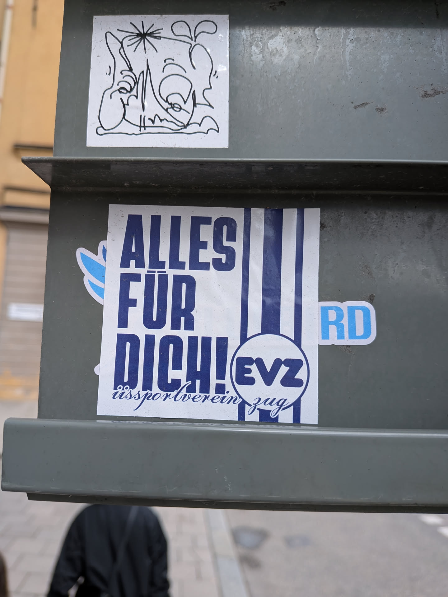 Street sticker The sticker features prominent blue text on a white background that reads 'ALLES FÜR DICH!' (Everything for you!). Below this, in a more script-like font, it says 'eßportverein zug'. A circular logo containing 'EVZ' is placed to the right of the main text. The sticker also has blue vertical stripes on the right side and a small blue wing-like graphic on the left. A separate small blue sticker with 'RD' is adjacent to the main sticker.