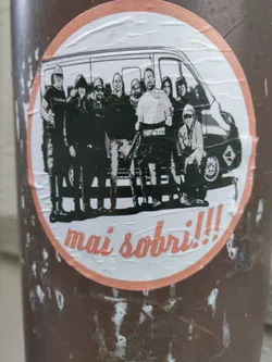 Street sticker A round sticker with a peach-colored border shows a black and white illustration of a group of people standing in front of a van. The text "mai sobri!!!" is written at the bottom of the sticker. 