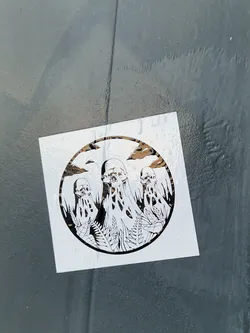 Street sticker The sticker displays a circular design with stark black line art on a white background, affixed to a dark, textured surface. The central motif consists of three grotesque, skull-like figures that appear to be melting or dripping, with elongated, organic shapes flowing from them. These figures are intertwined with intricate botanical elements, resembling leaves and ferns, suggesting an eerie blend of life and decay. The background within the circular frame shows subtle cloud formations. The overall aesthetic is dark, macabre, and illustrative, evoking themes of gothic art or dark fantasy.