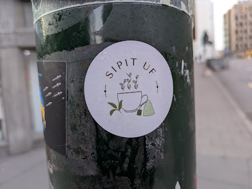 Street sticker A round sticker featuring a minimalist illustration of a cup of tea with tea bags and leaves. The text 'SIP IT UP' is written around the illustration.