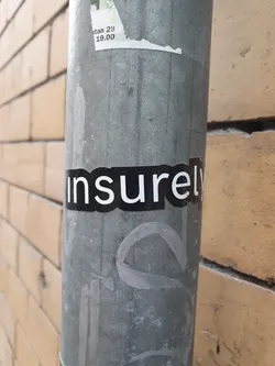Street sticker A black and white sticker with the word "insurely" on a grey metal pole. The sticker is slightly worn and there are other markings on the pole.