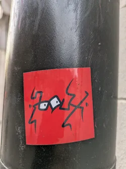 Street sticker The sticker features a red square with a black outline of a creature with eyes wearing glasses and zig-zagging limbs, creating a playful and somewhat whimsical appearance.