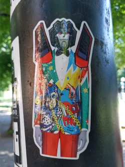 Street sticker A sticker featuring Megatron, the Decepticon leader from the Transformers franchise, dressed in a vibrant pop art-style suit. The suit is a collage of various patterns and characters. Megatron's head is visible at the top, and his signature weaponry is visible on his shoulders.  The overall aesthetic is a fun and unique blend of pop culture icons.