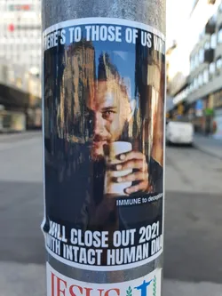 Street sticker A sticker featuring a stylized image of a man, possibly Tom Hardy, holding a cup. The text on the sticker suggests a celebratory or defiant tone toward closing out the year 2021.  The style is reminiscent of internet memes.