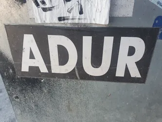 A black sticker with white capital letters spelling ADUR. The sticker is slightly dirty and weathered.
