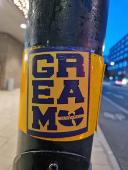 Street sticker A yellow and dark blue sticker featuring the stylized text 'GREMO' and the Wu-Tang Clan logo with 'SUNDSVALL' inscribed below it. The sticker is affixed to a dark pole outdoors.