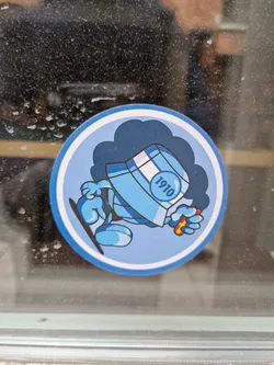 Street sticker A round sticker featuring a cartoon character. The character is light blue, wearing a bucket hat with "1910" written on it and appears to be holding a small orange object. It's set against a darker blue cloud-like background. The style is simple and slightly reminiscent of classic cartoon characters.