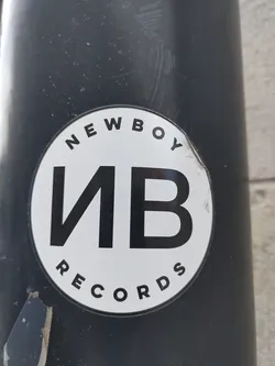 Street sticker A black and white circular sticker featuring the Newboy Records logo.  The logo consists of the abbreviation "NB" in bold black lettering within a white circle, with the words "NEWBOY" and "RECORDS" arched above and below respectively.