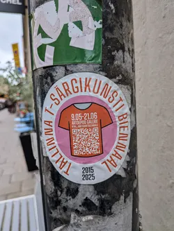 Street sticker An oval-shaped sticker with a white border featuring the orange text 'TALLINNA T-SÄRGIKUNSTI BIENNAAL' curved around the top and sides, and the years '2015' and '2025' printed in black at the bottom. The center contains a pink circle enclosing an orange T-shirt graphic. Inside the T-shirt illustration, white text lists the dates '9.05-21.06', the venue 'ARTDEPOO GALERII', and the Instagram handle '@TALLINNTSHIRTBIENNALE', above a large QR code.