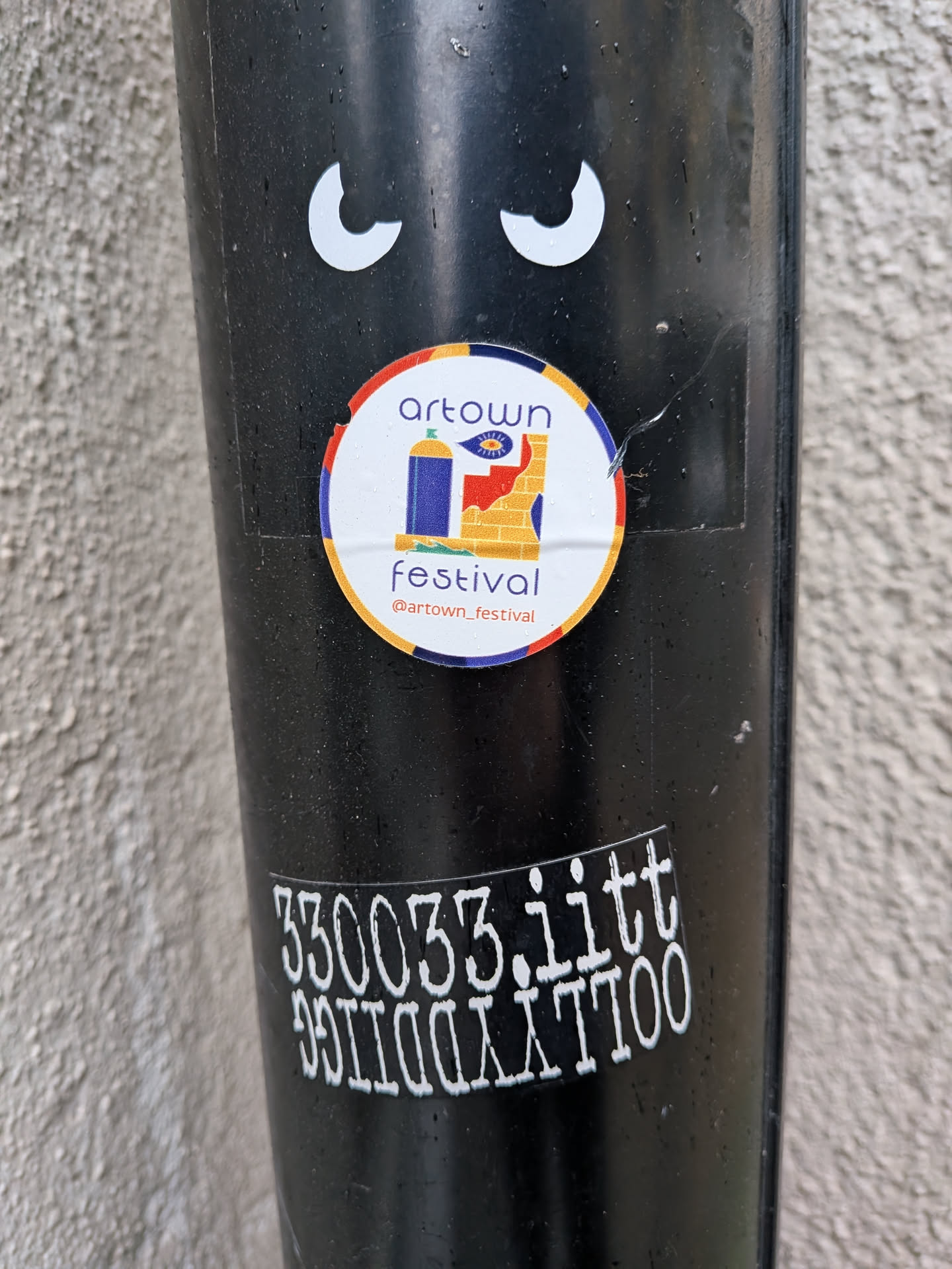 A circular sticker featuring a colorful illustration. It has an outer orange-red ring, followed by a blue ring, and a white central background. The main graphic depicts a blue spray paint can with a green nozzle on the left, next to a red and yellow brick wall on the right. An eye symbol is visible on the yellow section of the wall. Above the illustration, 'artown' is written in purple, and below it, 'festival' is in red, followed by '@artown_festival' in purple.