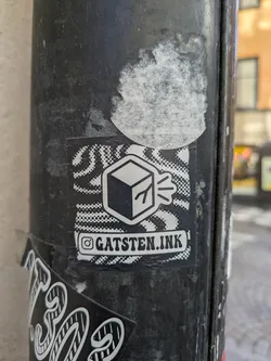The sticker displays a white cube with tree branches coming out of it, set against a background of halftone-style patterns. Below the design is text indicating the Instagram handle. The sticker is affixed to a weathered pole, with parts of another sticker visible underneath.