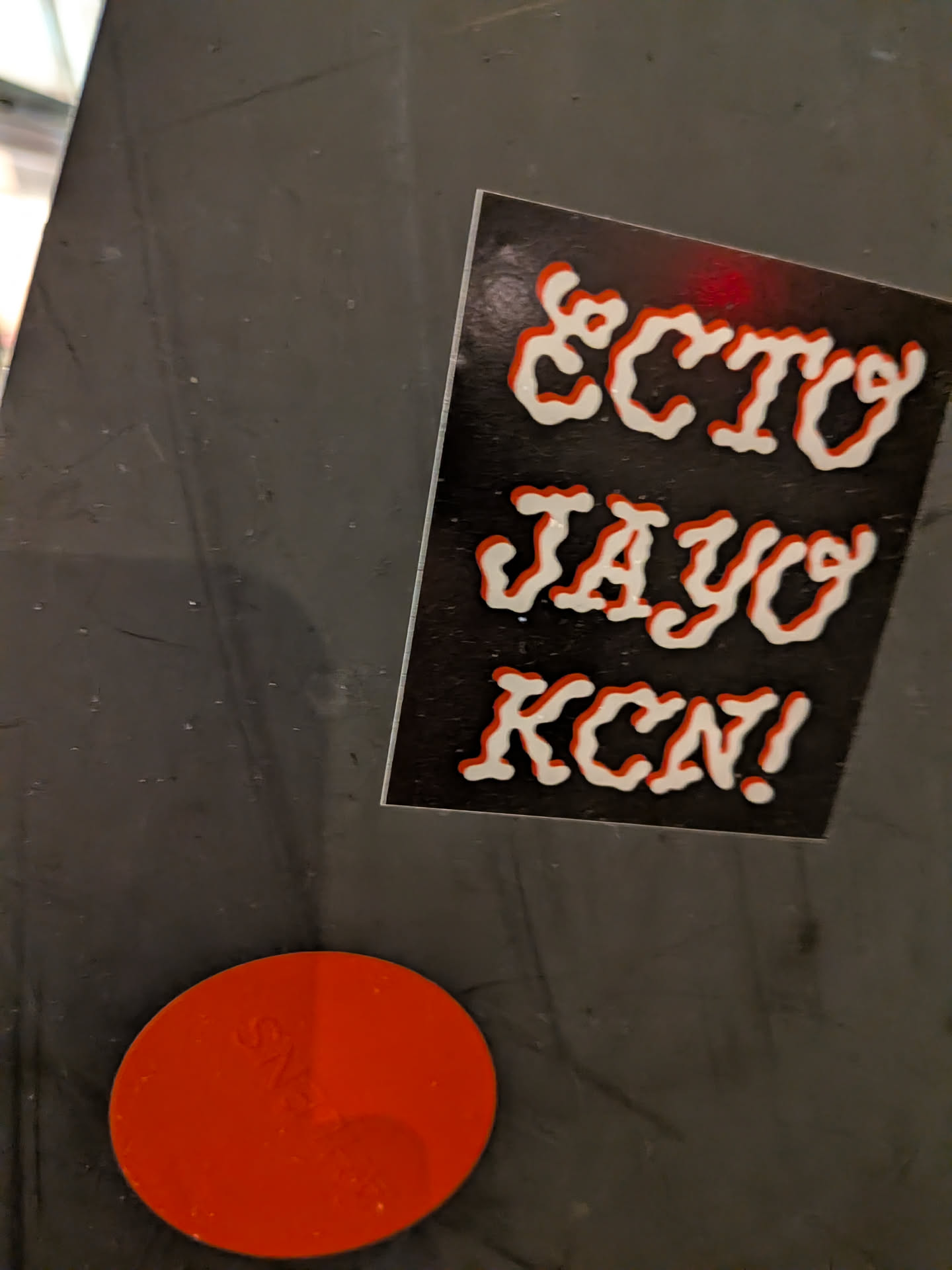The sticker is rectangular with a black background. It features three lines of text in a bold, stylized font. The letters are filled with white and have a prominent red outline, giving them a raised, almost 3D appearance. The text reads 'ECTO', 'JAYO', and 'KCN!' from top to bottom. There is a faint red smudge above the 'ECTO' text.