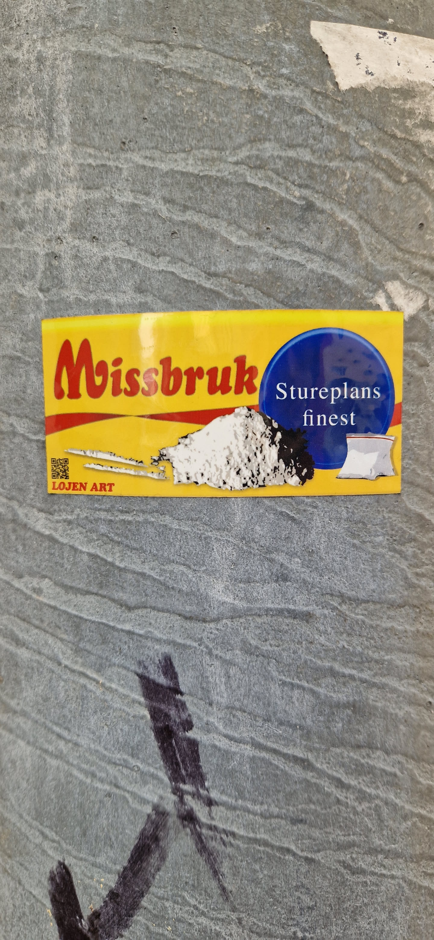 The sticker is yellow with red lettering spelling "Missbruk". A blue circle contains the text "Stureplans finest" in white.  Below, there is an illustration of what appears to be a pile of a white powdery substance with two lines and a small bag next to it. A small QR code is placed at the bottom left corner, along with the text "LOJEN ART".