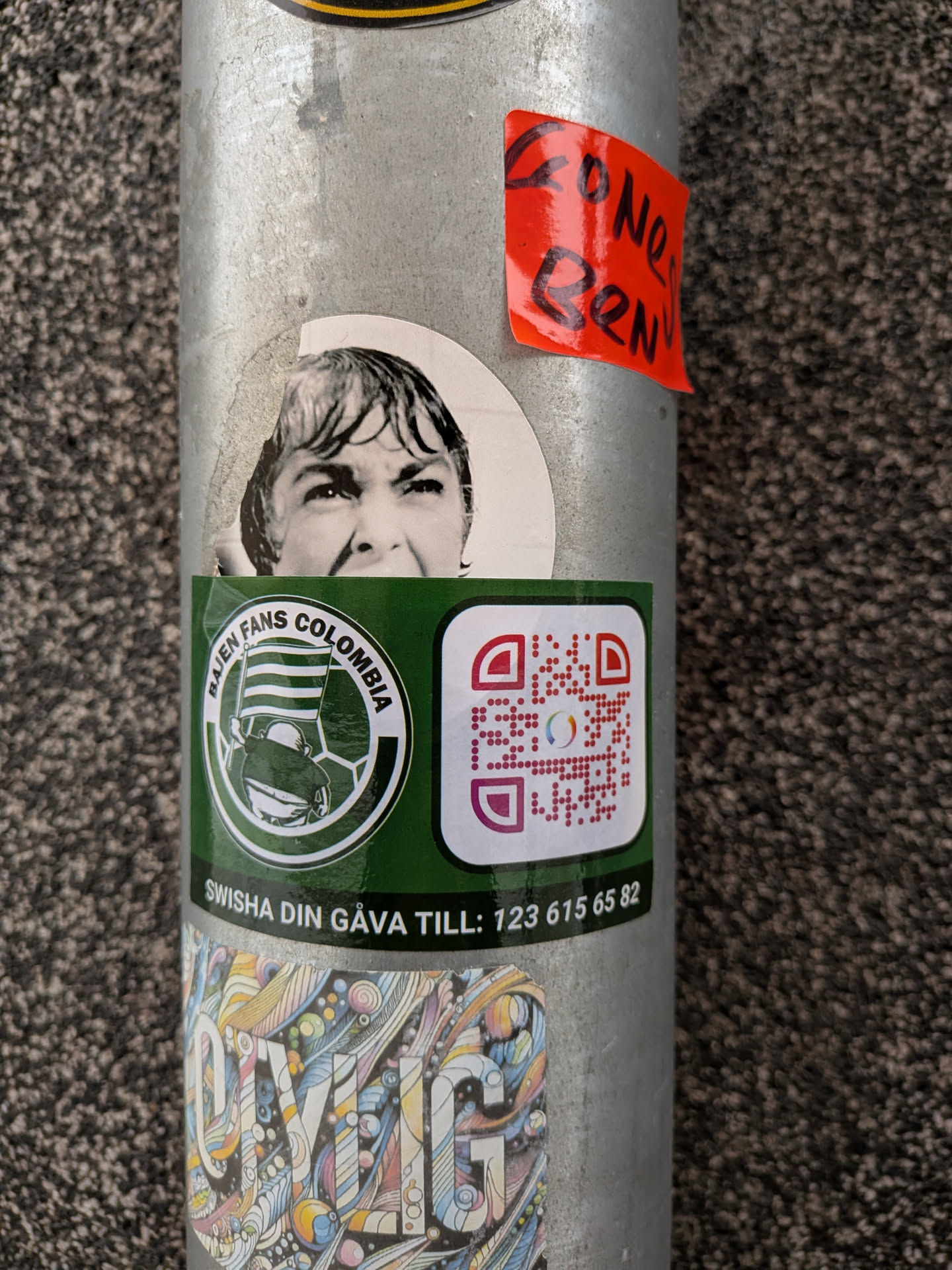 Street sticker A rectangular green sticker featuring a circular white logo with a green border. Inside the circle, a stylized figure holds a striped flag (green and white), resembling a football fan. The text 'BAJEN FANS COLOMBIA' is written around the top of the circle. To the right of the logo is a square QR code with a white background and red/purple pixels, featuring a small colorful circular logo in its center. Below these elements, the text 'SWISHA DIN GÅVA TILL: 123 615 65 82' is printed in white.