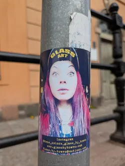 Street sticker The sticker features a woman with striking eyes and pink and purple hair. She is wearing a hat with the words 'Glass Art' on it. At the bottom of the sticker, there's an Instagram handle, a website address, and an email address.