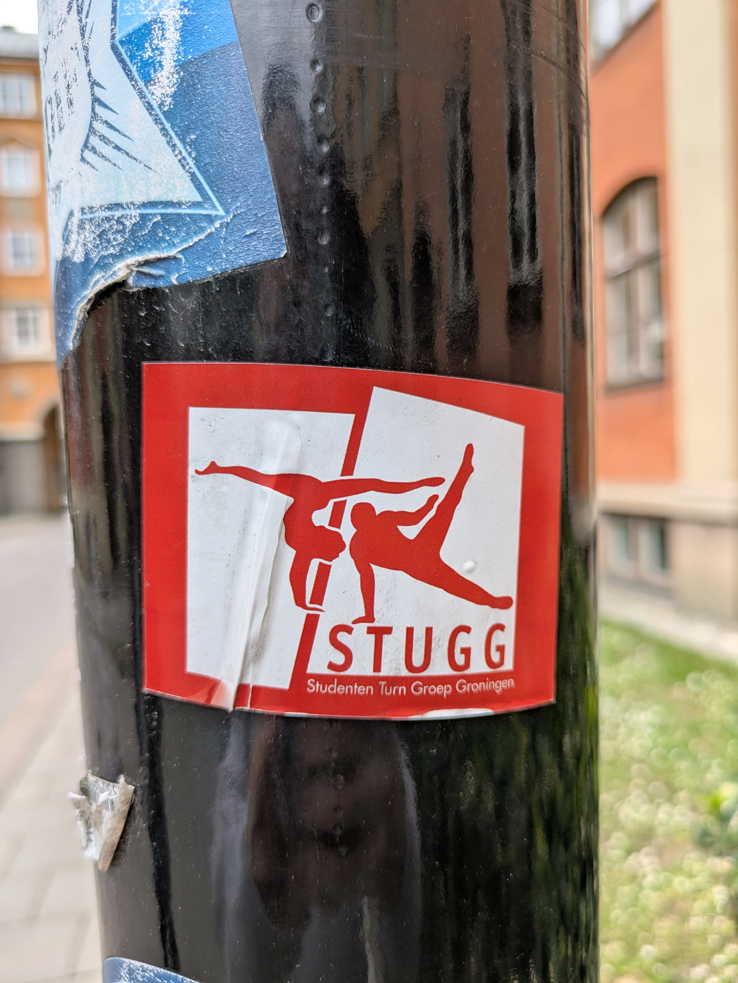 This is a sticker for STUGG, the student gymnastics group of Groningen. The design features two gymnasts in red silhouettes against a white background, set within a red square.