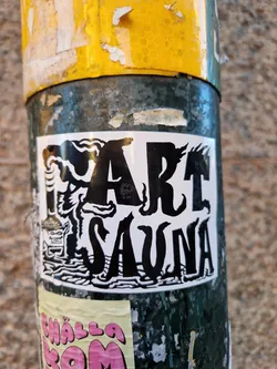 Street sticker A black and white sticker with the words "Fart Sauna" in a stylized font. The design includes a small illustration of what appears to be a sauna building and steam or smoke.  The sticker is affixed to a weathered pole.