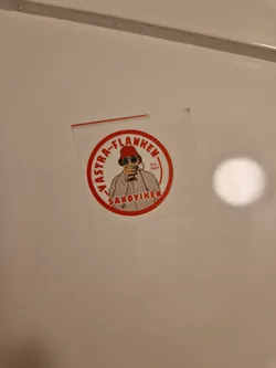 A round sticker with a red border and white background. It features an illustration of a person wearing a red bucket hat, sunglasses, and a light-colored jacket, holding a drink. The text "VäSTRA-FLANKEN" is written in a circle around the illustration, with "SANDVIKEN" written below.  The year "Est. 2007" is visible.