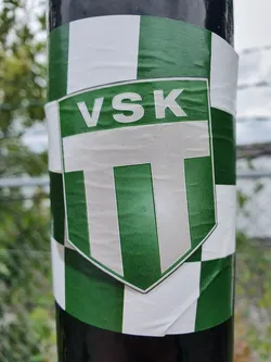 Street sticker A green and white sticker featuring the logo of VSK Tennis club. The logo is a shield shape with vertical stripes and the abbreviation VSK in the top part. The background of the sticker is a checkered pattern of green and white squares.
