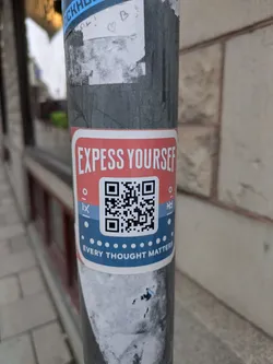 A sticker with a QR code promoting self-expression. The colors are predominantly red, white, and blue. The QR code is surrounded by small dots. The text is clear and legible.