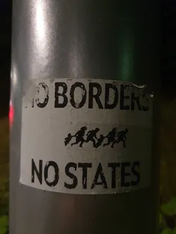 A sticker with the text "NO BORDERS NO STATES" and an illustration of people running. It's attached to a gray pole.