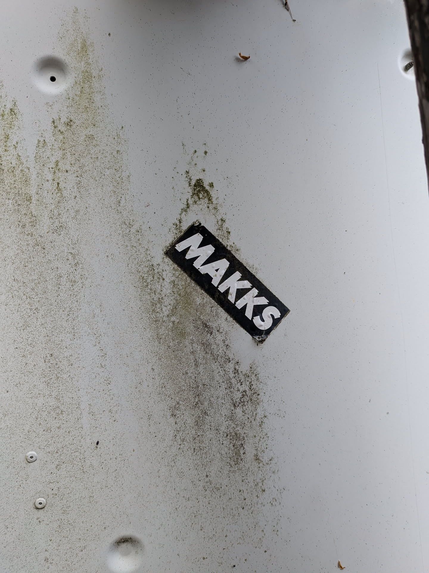 A diagonal rectangular sticker with a black background and bold white 'MAKKS' text, stuck on a dirty white surface.
