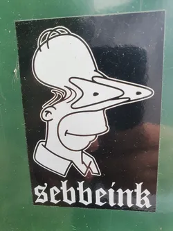 Street sticker Black and white sticker featuring a distorted illustration of Homer Simpson with three noses.  The artist's name, "Sebbeink", is printed in a gothic-style font below the image.
