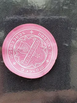 A round pink sticker with a white design. The design includes a Nordic-style emblem, crosses, and text that appears to say "2023 Nordisk".  The style is reminiscent of vintage or traditional Nordic imagery. 
