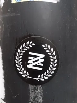 Street sticker A round black sticker with a white laurel wreath encircling a stylized letter 'N' logo. The logo consists of three vertical, parallel lines forming the shape of a letter 'N'.