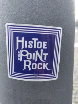 A sticker featuring the text "Histoe and Point Rock" in a stylized font within a blue square frame. The sticker is affixed to a grey pole.