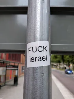Street sticker A square white sticker with black sans-serif text reading 'FUCK israel' on a metallic pole.