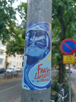 Street sticker A sticker featuring a stylized illustration of a person wearing sunglasses, seemingly inspired by the movie Fear and Loathing in Las Vegas. The sticker has a blue and yellow color scheme with a wave-like design. The text 'Fear & Loathing in Stockholm' is prominently displayed.