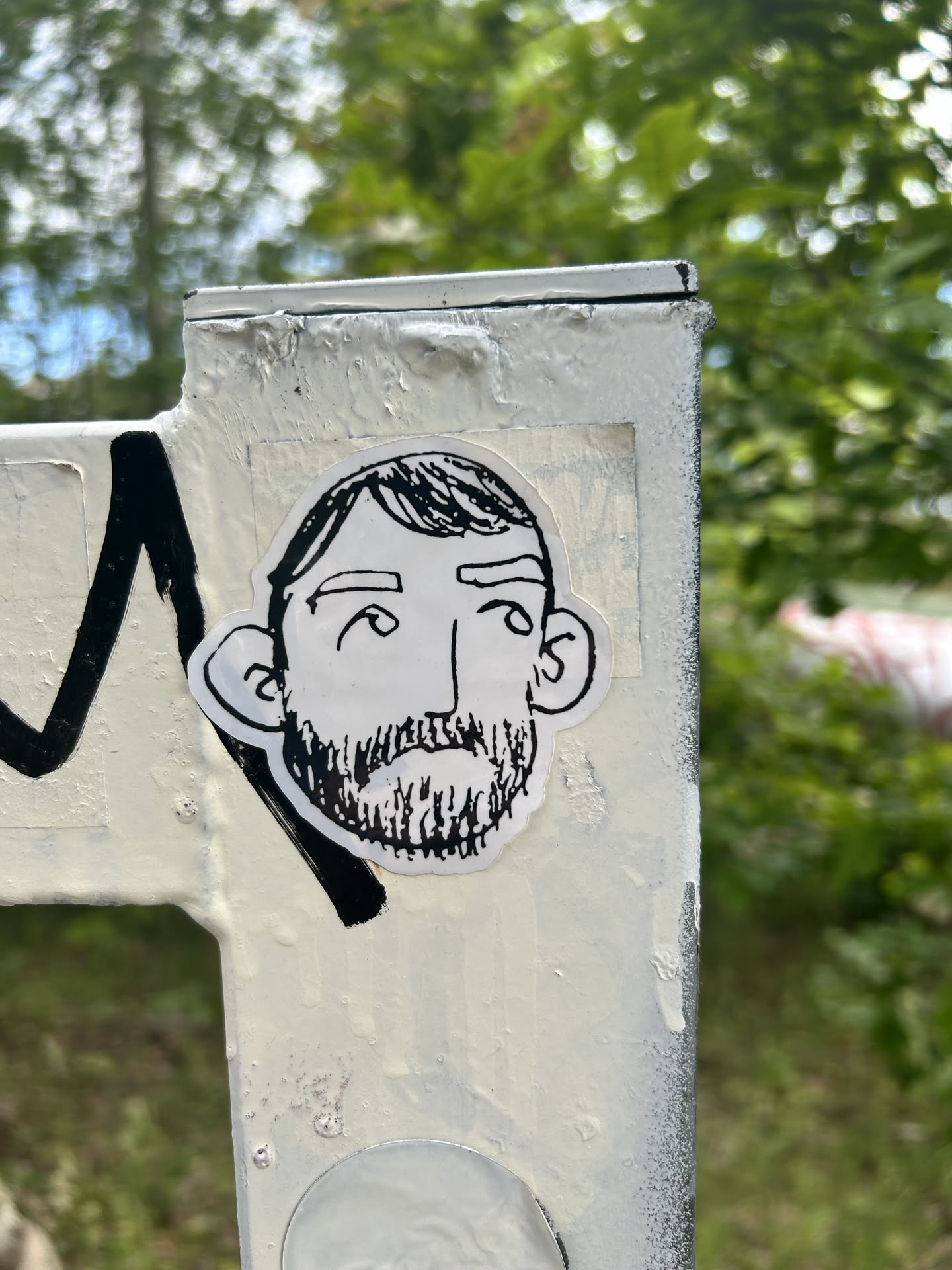 Die-cut sticker featuring a simple black ink line drawing of a man's face with a full beard, short hair, and prominent ears on a white background.
