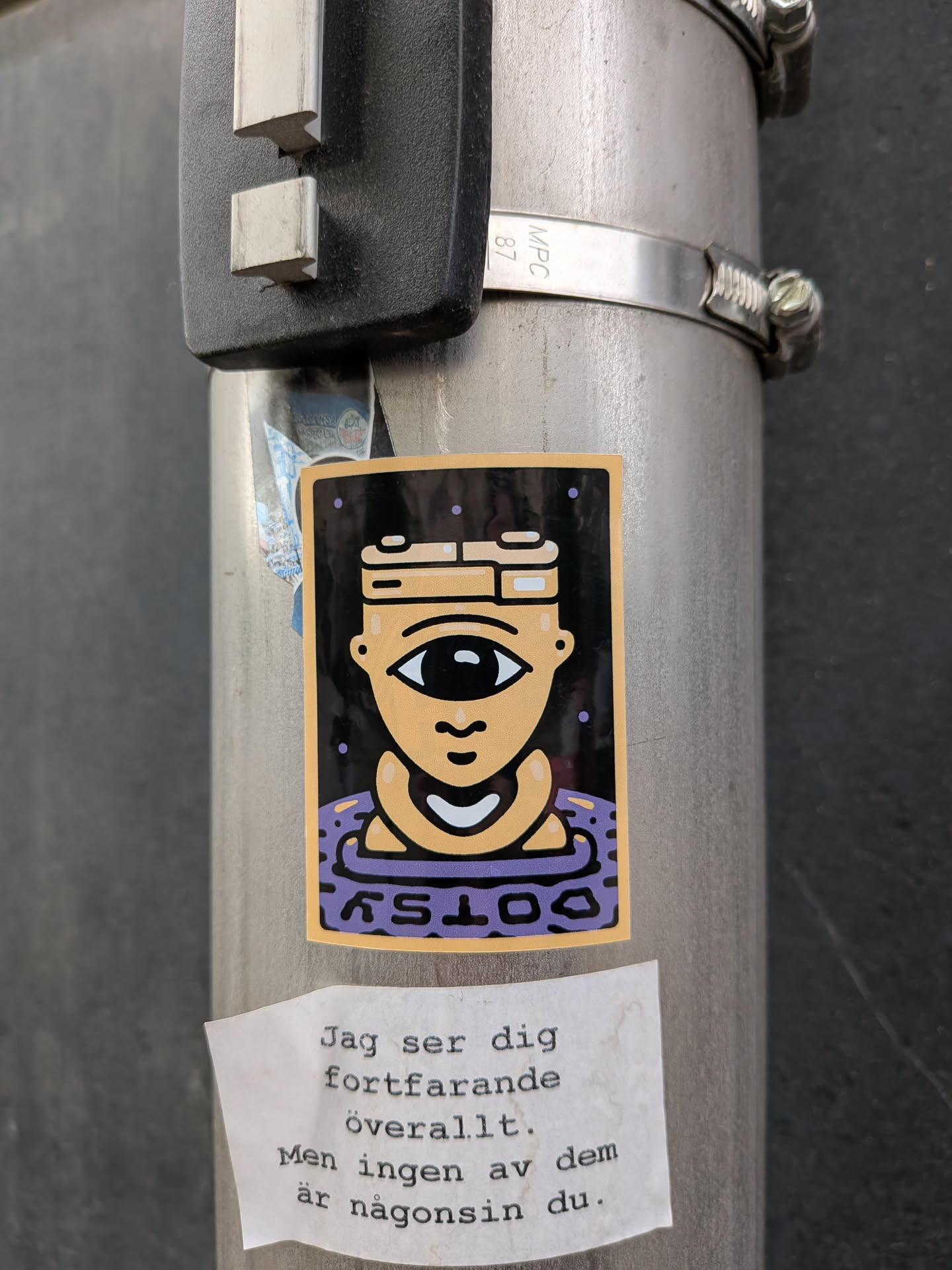 A rectangular sticker depicting a tan cyclops character with a camera-shaped head. The character floats in a purple ring labeled 'COTSY' against a dark, dotted background.