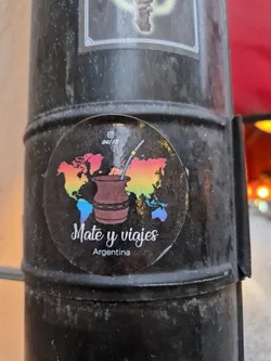Street sticker Round sticker featuring a yerba mate cup on a rainbow world map. The text says "Mate y viajes Argentina".