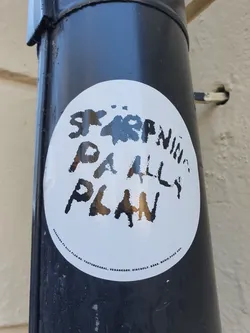 Street sticker A white oval sticker with the text "Spare Plan" written in a stylized, hand-drawn font. Smaller text at the bottom appears to be website or contact information. The sticker is affixed to a dark-colored cylindrical object, possibly a pipe or pole.